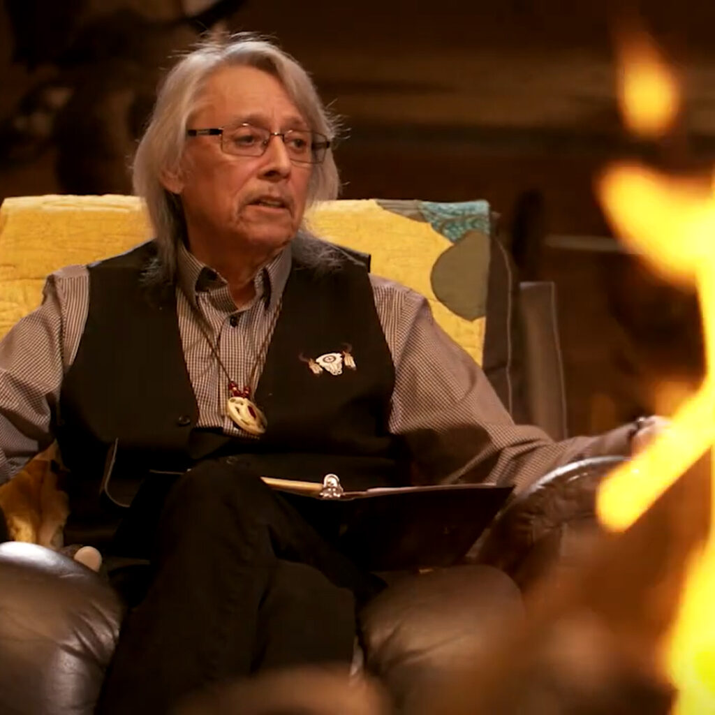 Elder Dave Courchene sitting with fire in front of him.