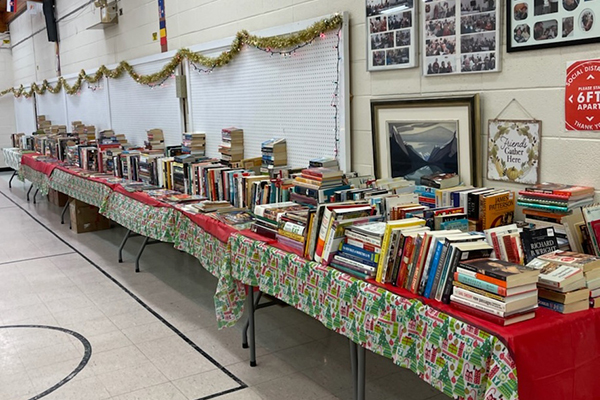 Many long table lined up that have stacks of books on top of them.