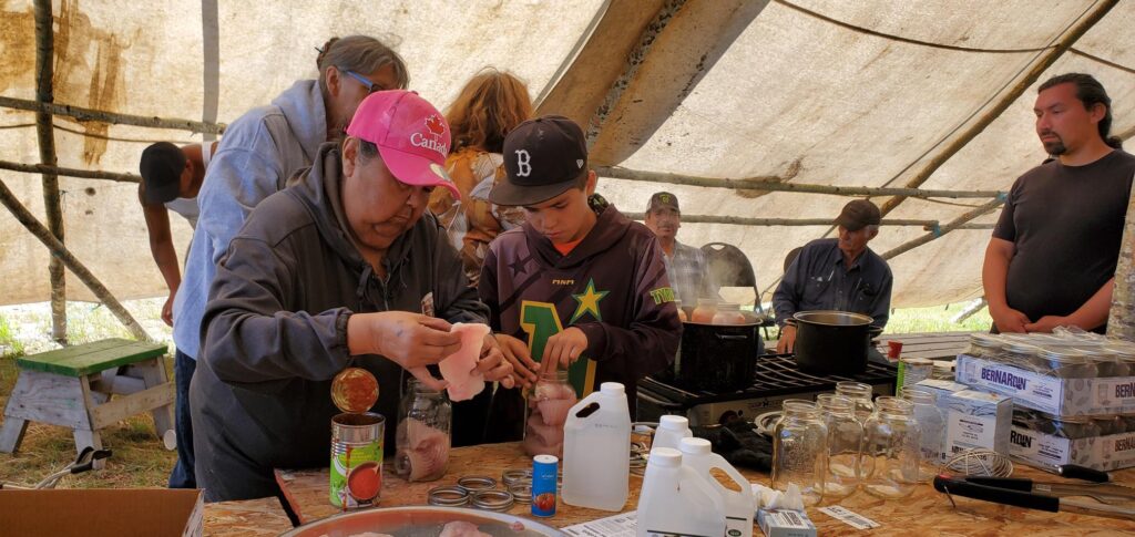 An adult and youth in baseball hats can fish at a table covered in mason jars inside a canvas tent.