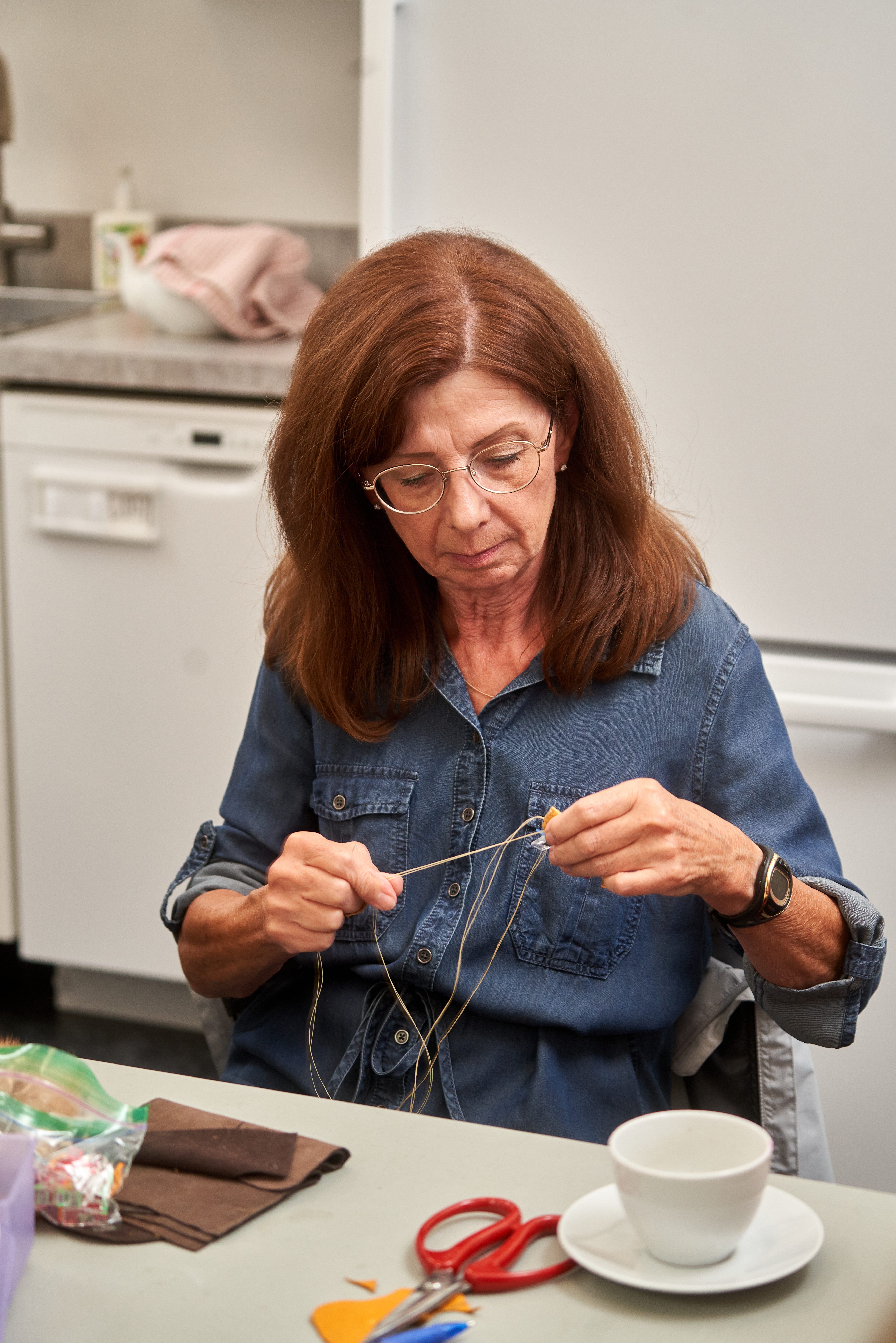 A woman in a denim shirt measures out a length of thread.