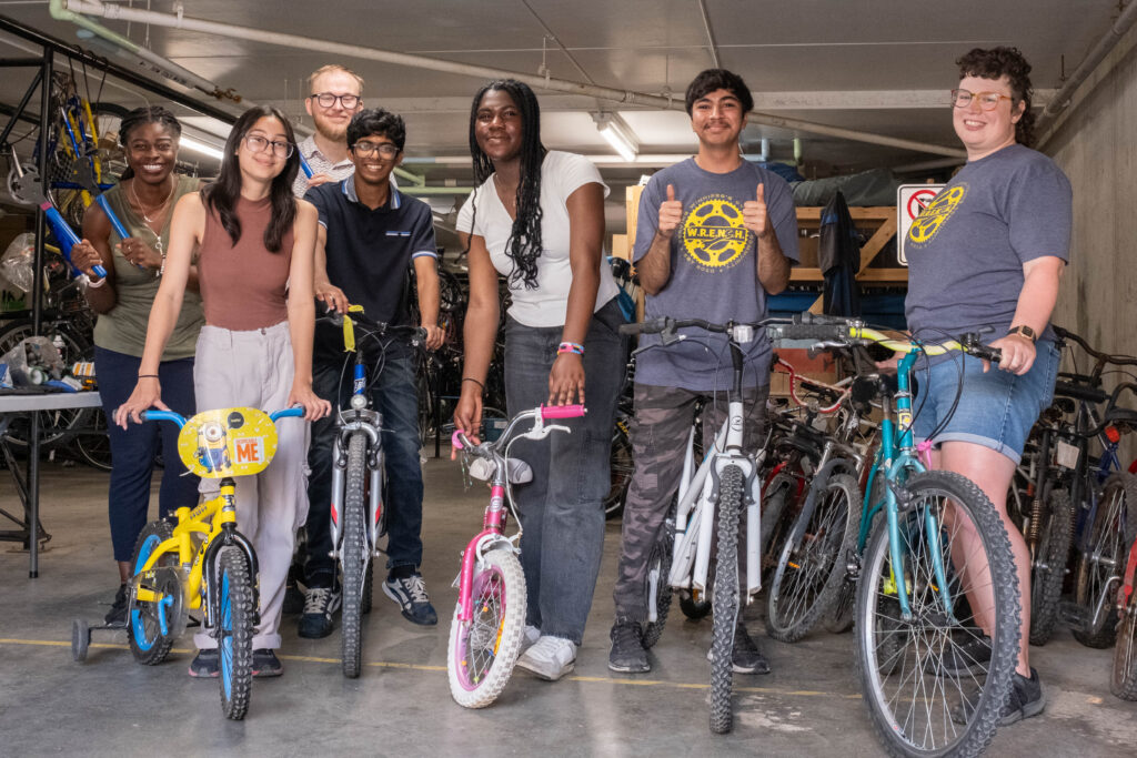A group of Summer Internship Program participants stand with bicycles at The WRENCH.