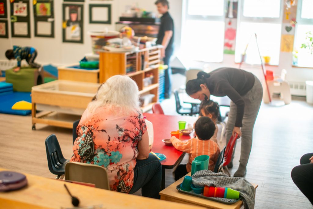 Adults and young children gather around a table inside a bright early childhood learning and play space.
