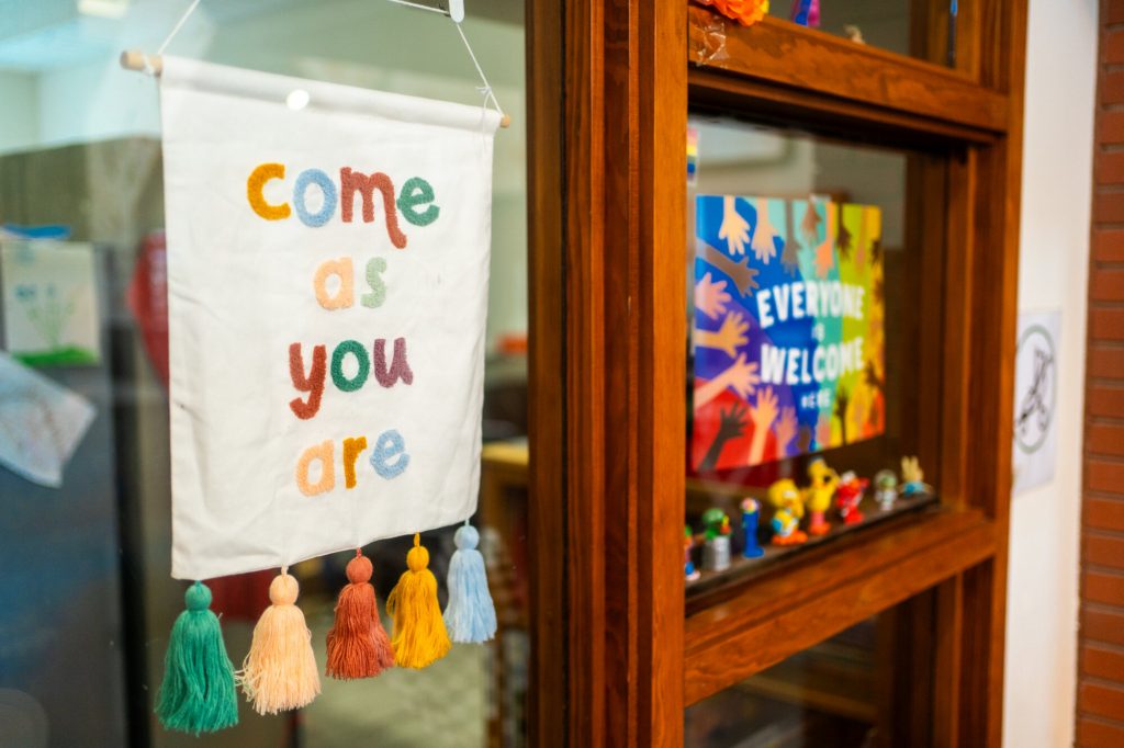 A handmade sign reading “Come as you are” hangs beside a colourful “Everyone is Welcome” poster.