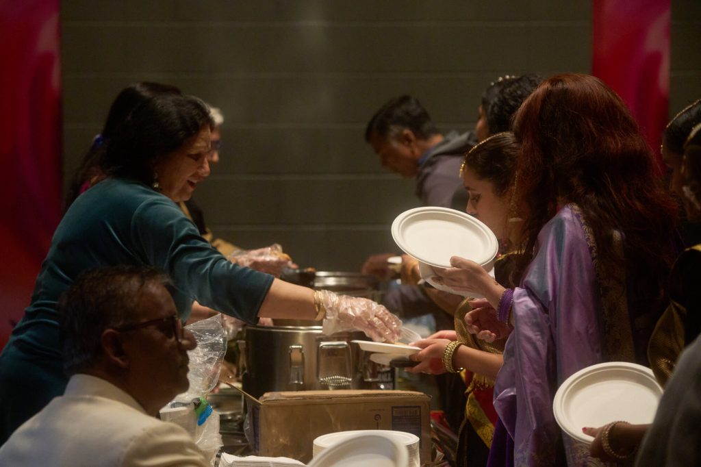 Four women stand behind serving dishes at a community cultural event.