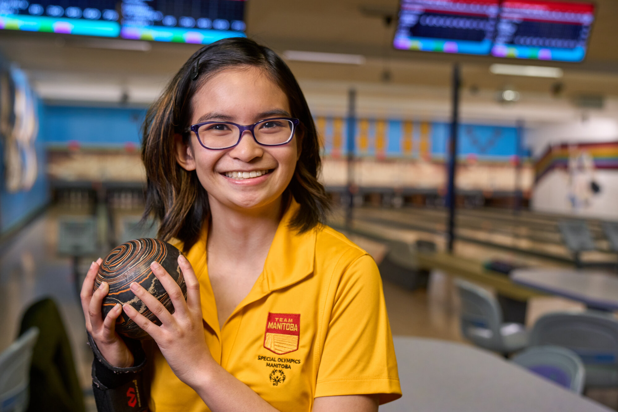 Elizabeth Dela Cruz smiles while holding a bowling ball at a bowling alley.