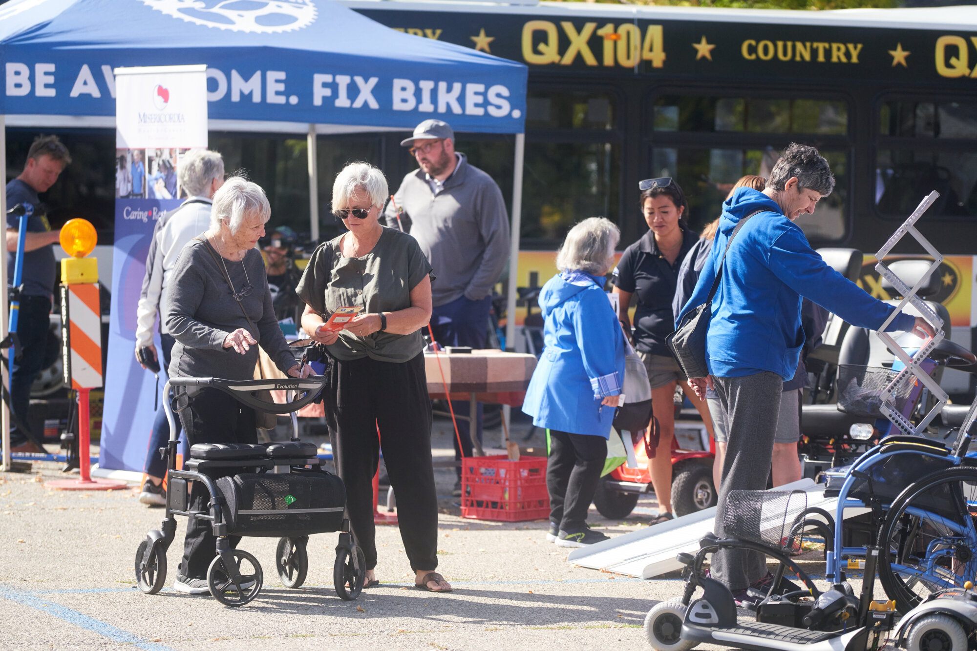 People gather outdoors at a community accessibility fair while browsing mobility equipment and community resource booths.
