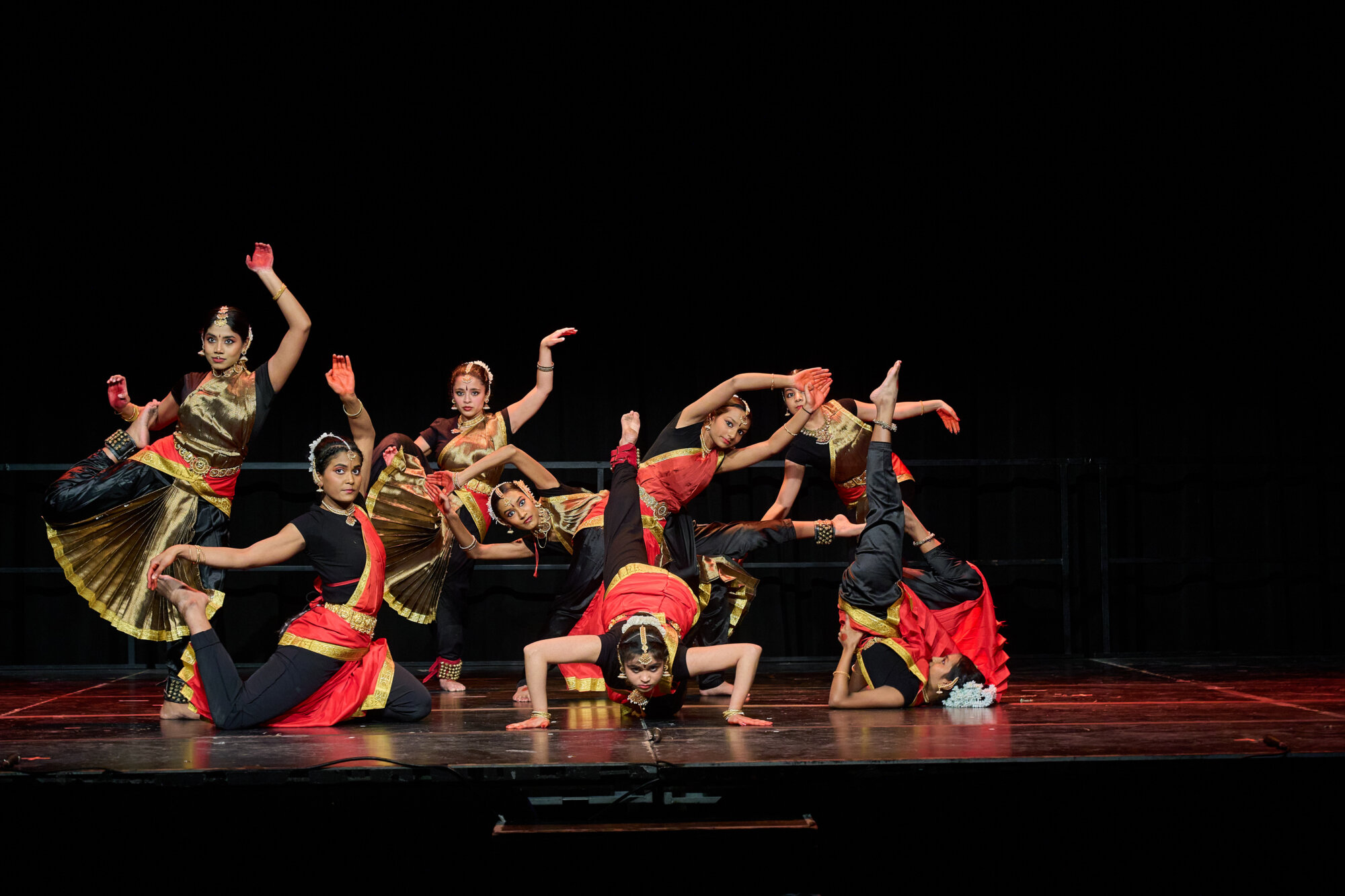 A group of dancers in coordinated red and black costumes perform on stage.