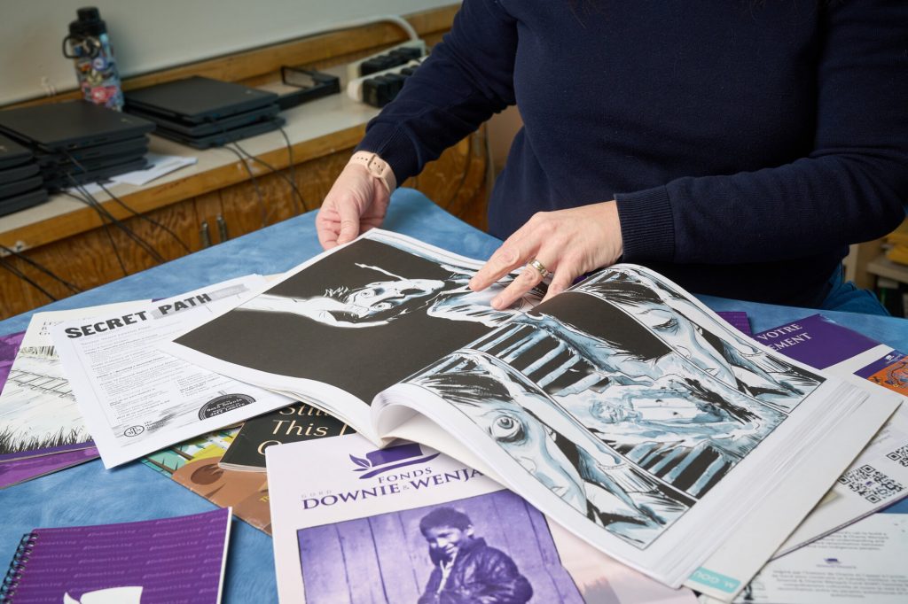 A person flips through pages of Secret Path surrounded by reconciliation and educational resources on a table.