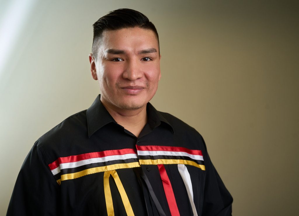 A man wearing a black shirt with red, gold, white, and black ribbon detailing.