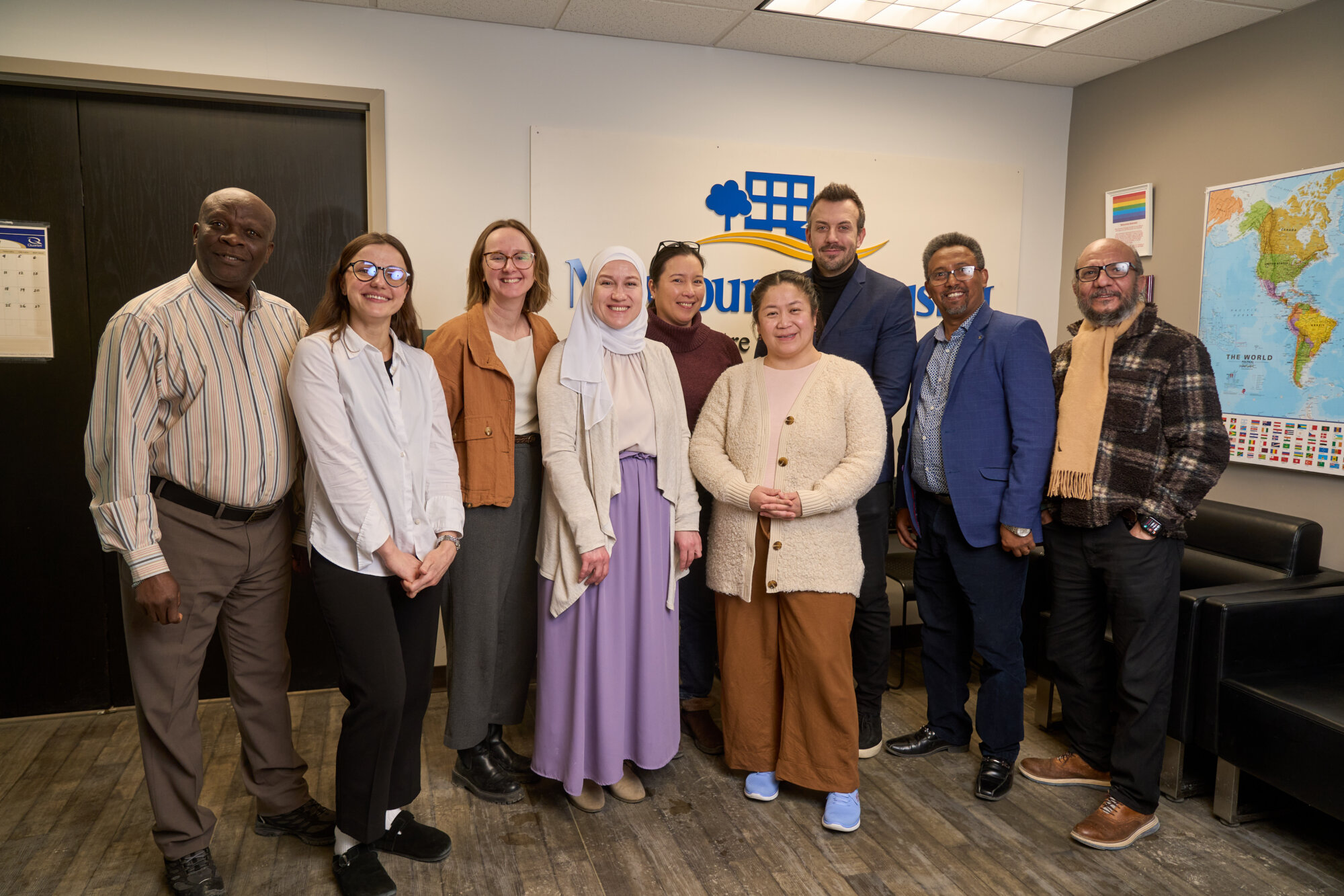A group of community members and staff stand together inside the New Journey Housing office, smiling in front of the organization’s sign.