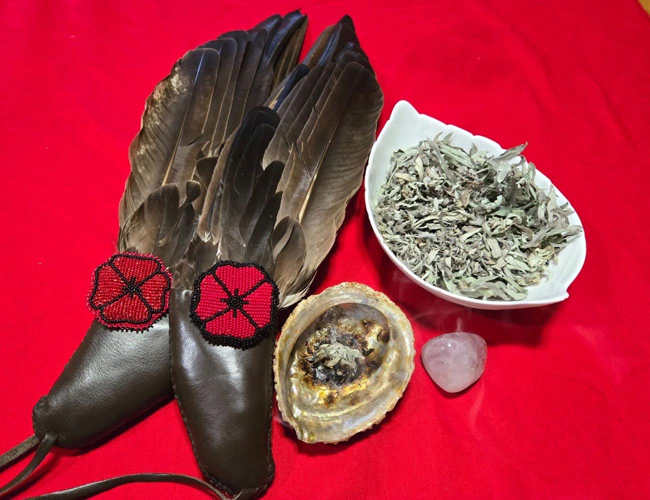 Feathers, medicines, and ceremonial items are displayed on a red cloth.