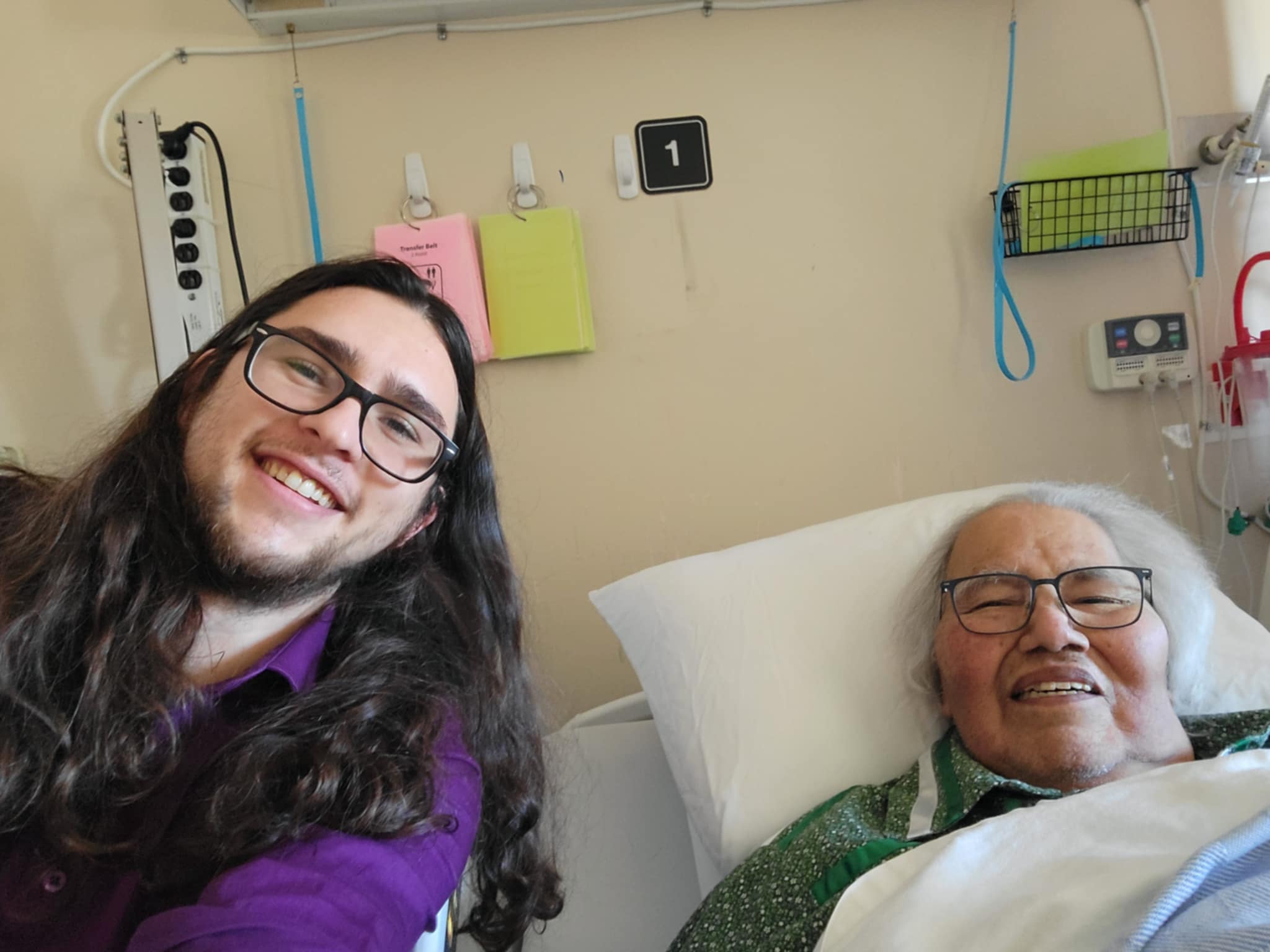 A young man smiles beside Murray Sinclair in a hospital room.