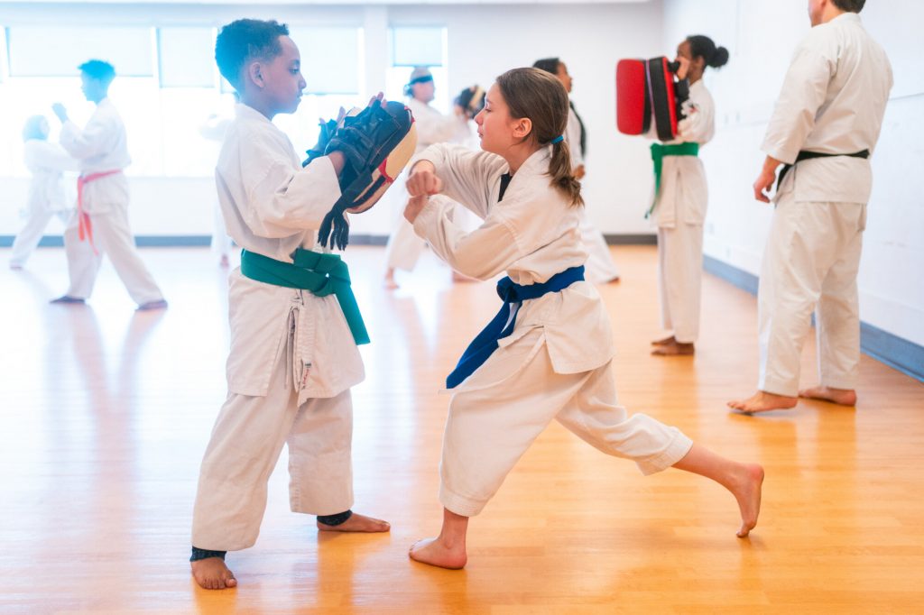 Two children in karate uniforms practice punches during a martial arts class.