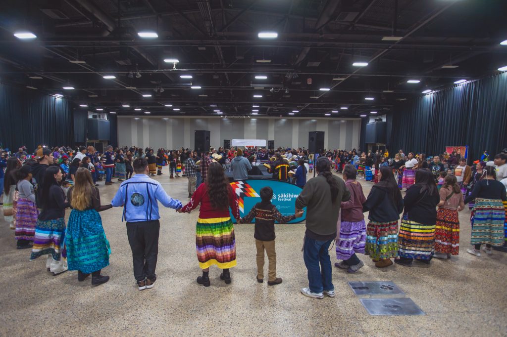 Image of people gathering in a circle at the Murray Sinclair Memorial Round Dance - Photo courtesy of sākihiwē festival. Taken by Nadya Kwandibens.